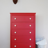 A tall red dresser with silver and white knobs