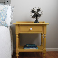 A mustard yellow nightstand with a milk glass knob